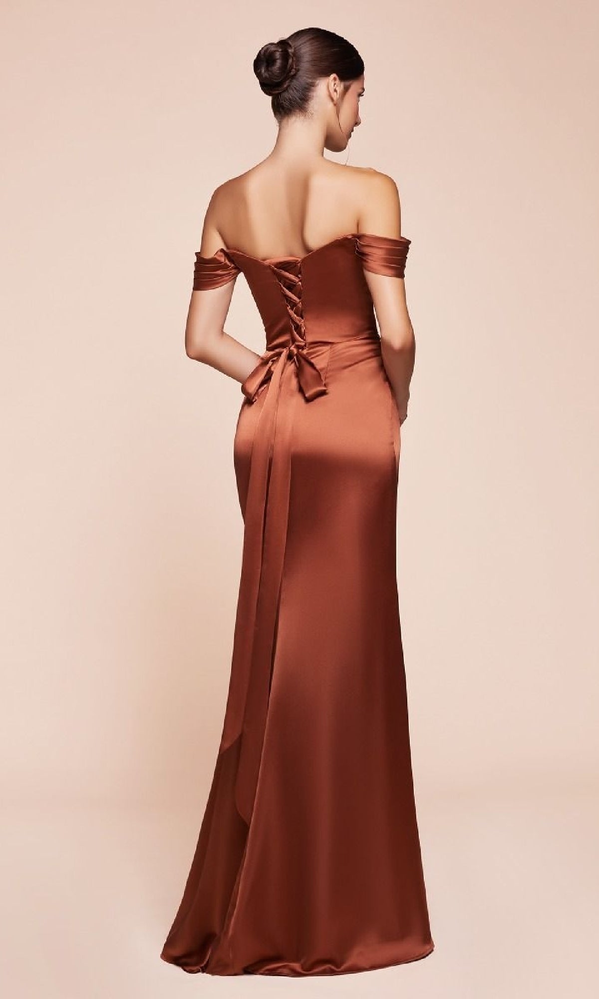A woman wears the affordable Lace-Up Off-Shoulder Prom Dress: Ladivine 7452, a floor-length copper satin gown with a sash and lace-up back, standing against a plain beige background—perfect for any special occasion.
